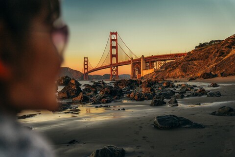 An adult looking out across the water to the Golden Gate Bridge from Marshall's Beach, San Francisco.